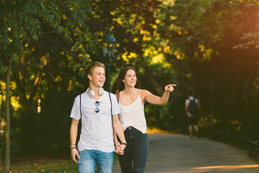 Teenage couple walking in Stadtpark in Vienna. Holding hands and enjoy in beautiful sunset. Girl pointing on something. Caucasian couple born in Vienna, Austria.