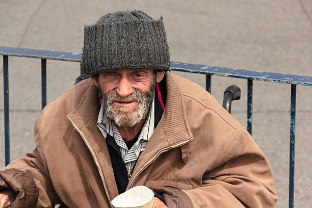 Homeless man in wheelchair holding paper cup stock photo