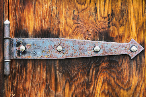 Rusted hinge hardware against deeply grained cedar wood panel door.