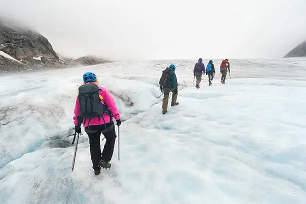 Five people wearing helmets and crampons are trekking over ice on an overnight adventure on Lemon Glacier, Juneau Icefield, Juneau, Alaska, USA