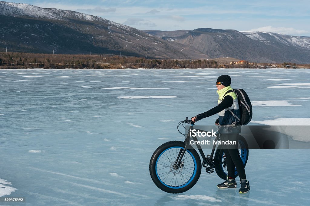 Fatbike. Fatbike (also called fat bike or fat-tire bike) - Cycling on large wheels. Cyclist holding a bike, and watching the sunset. They are standing on the frozen lake. Cycling Stock Photo