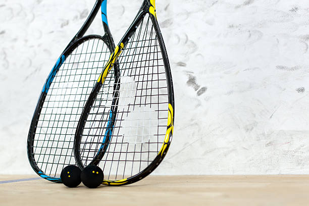 Two tennis rackets and balls standing by the wall Close up of two tennis rackets and black balls over white wall background - sport, fitness, healthy lifestyle and objects concept squash stock pictures, royalty-free photos & images