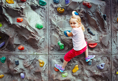 Skillful little girl enjoying climbing on the wall with grips for feet and hands