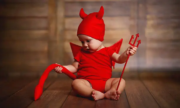 Photo of funny baby in devil halloween costume on wooden background