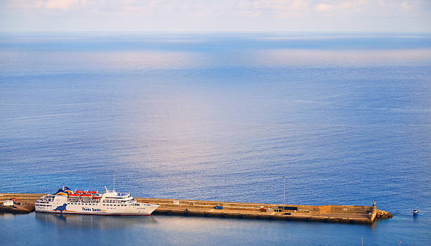Porto Santo, Portugal - August 17, 2016: The Porto Santo line ferry Lobo Marinho in Porto Santo's main harbour. Way out on the horizon we can just see the white sail of a yacht.