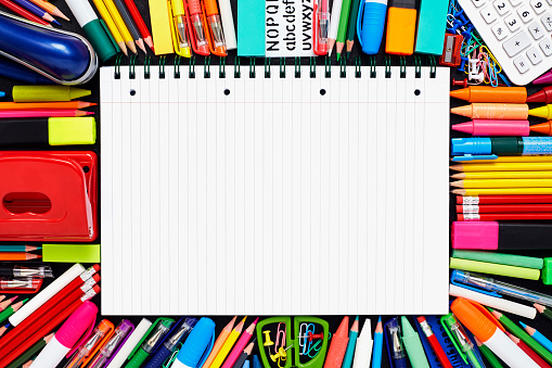 Close-up of blank spiral notebook. Notepad is surrounded by school supplies. They are kept on blackboard.