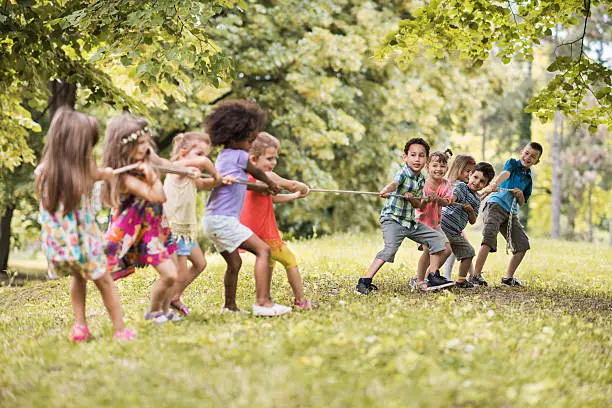 Large group of playful kids having fun in the park while playing tug-of-war.