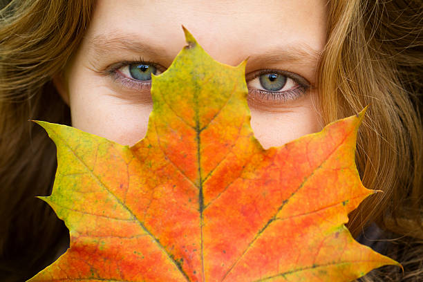 Young woman covered her face with autumn leaves