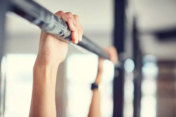 Close-up of hands holding pull-up bar. Woman is exercising in health club. She is in brightly lit gym.
