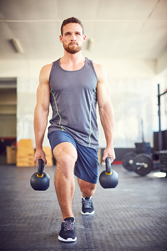 Determined male athlete lifting kettlebells in gym. Young fit man is exercising in health club. He is in sports wear.