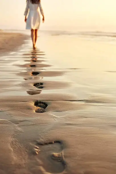 Photo of Woman walking barefoot on wet shore leaving footprints in sand