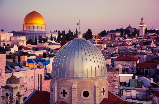 A view of rooftops of Old City of Jerusalem at sunset. Grey dome of Church of Our Lady of the Spasm (Armenian church) and golden Dome of the Rock.