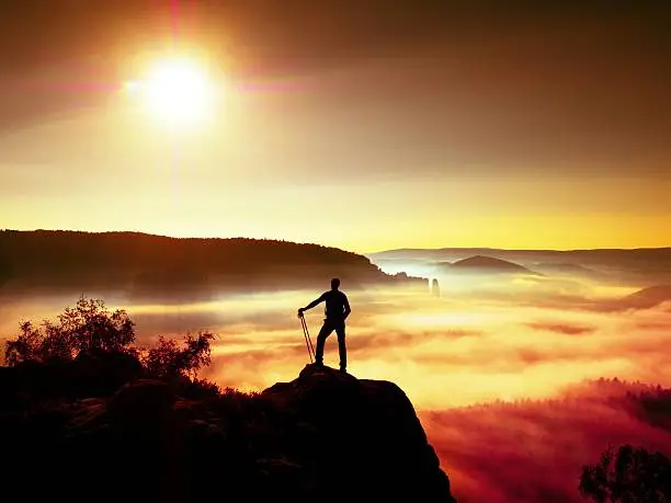 Photo of Tall backpacker with poles in hand. Sunny daybreak in rocks