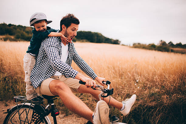 Biking with my dad Little boy and his father are riding a bicycle outdoors in the nature hipster bike stock pictures, royalty-free photos & images