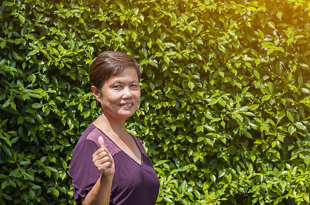 старшая азиатская женщина показывает большие пальцы вверх. - hand sign human hand ok sign grass стоковые фото и изображения
