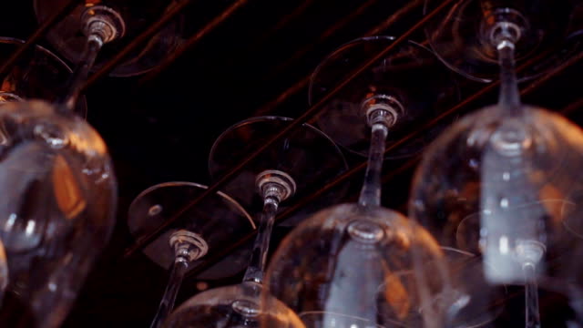 Cleaned glowing wine glasses hang at bar stand. Restaurant. Reflection