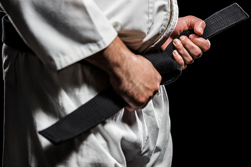 Close-up of fighter tightening karate belt on black background