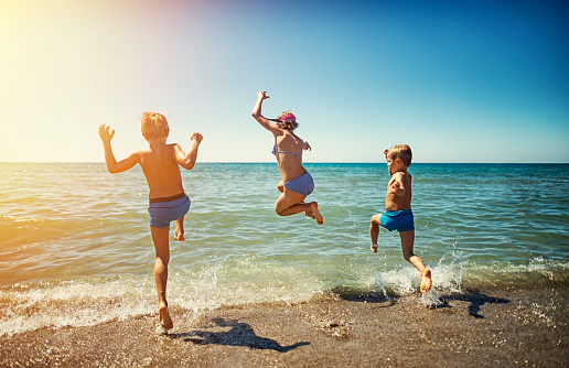 Three kids - a girl and two boys  - are having fun in sea.  Kids are jumping in the sea. Sunny summer day in Tuscany, Italy. Beautiful sandy beach in Tirrenia.