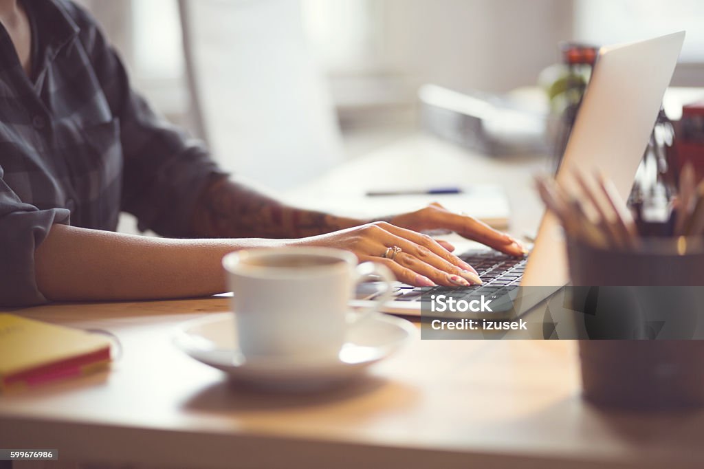 Woman using laptop at home, close up of hands Woman sitting at the desk and using a laptop in an office or at home, close up of hands, unrecognizable person. Adult Stock Photo