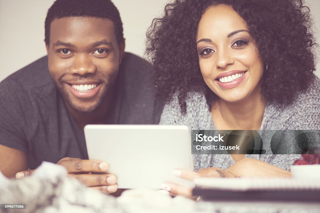 Afro american happy couple using a digital tablet Afro american friendly couple lying on bed at home and using a digital tablet, smiling at camera. Close up of faces. Adult Stock Photo