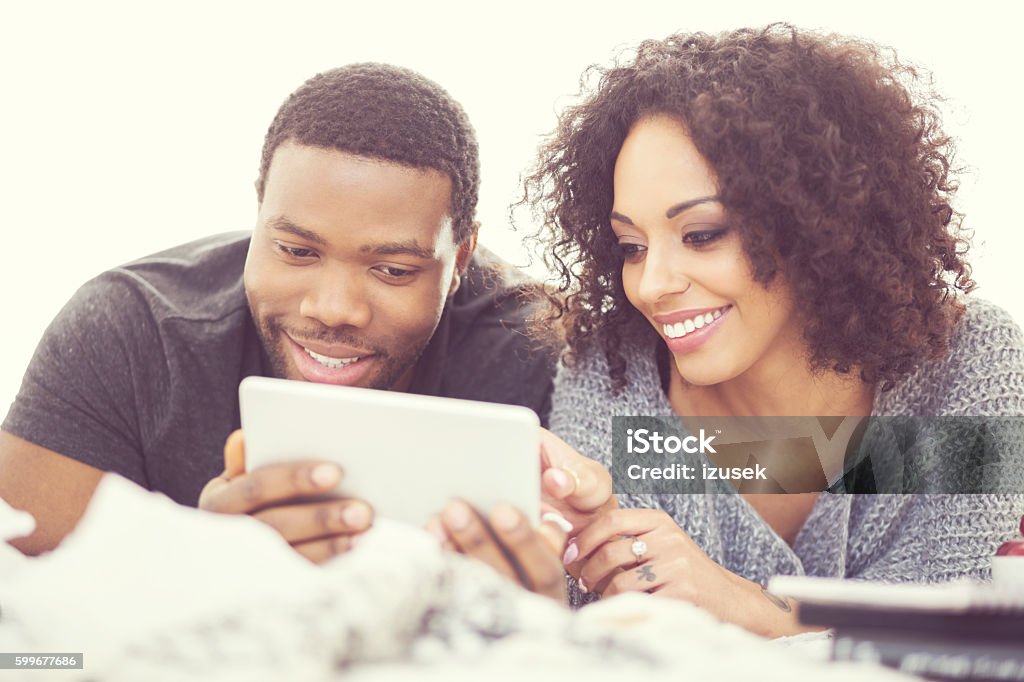 Afro american couple using a digital tablet Afro american friendly couple lying on bed at home and using a digital tablet. Close up of faces.  Adult Stock Photo