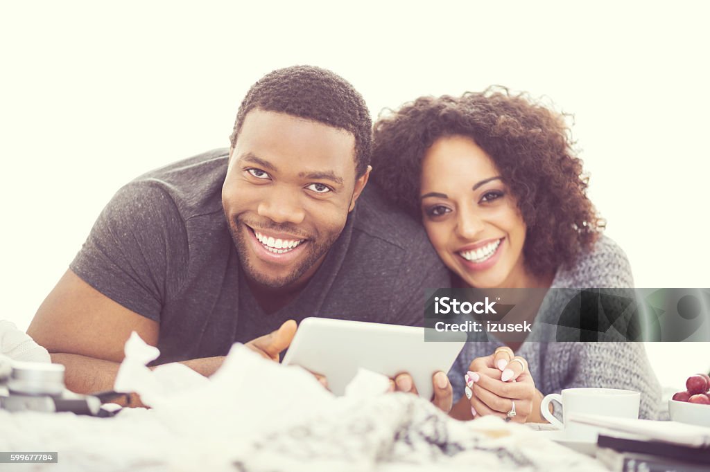 Afro american happy couple using a digital tablet Afro american friendly couple lying on bed at home and using a digital tablet, laughing at camera. Close up of faces. Couple - Relationship Stock Photo
