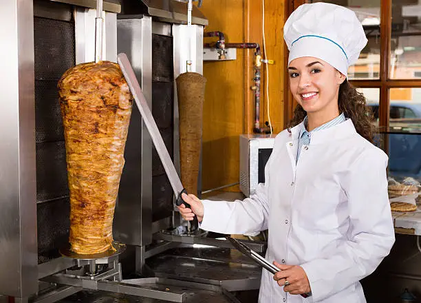 Photo of Professional female cook with grilled meat on spit for kebab