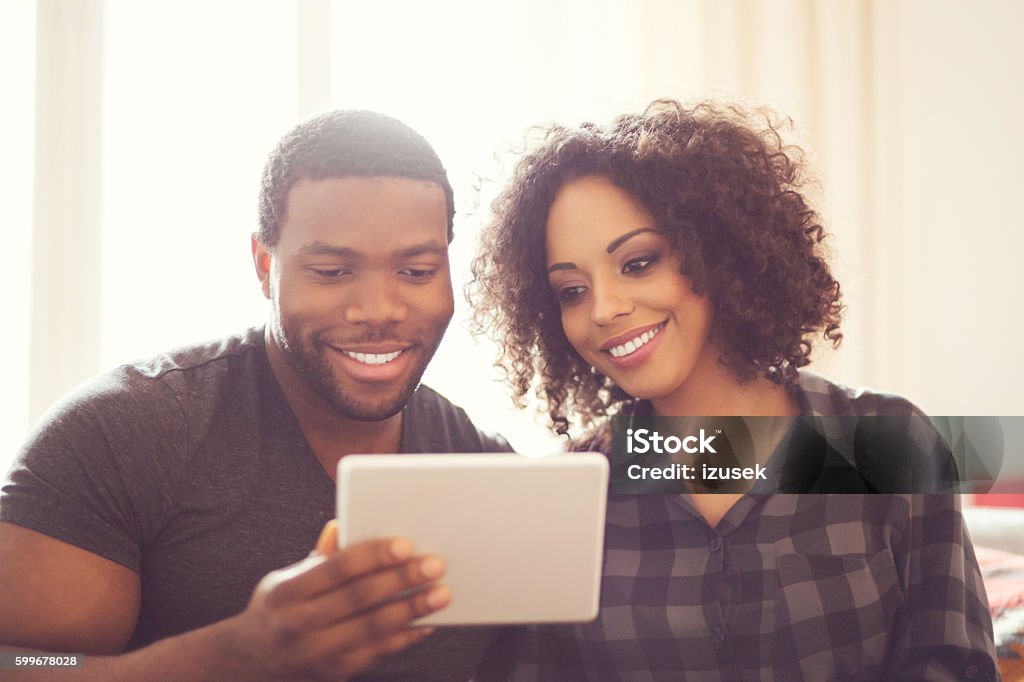 Afro american happy couple using a digital tablet at home Afro american friendly couple sitting on sofa at home and using a digital tablet. Digital Tablet Stock Photo