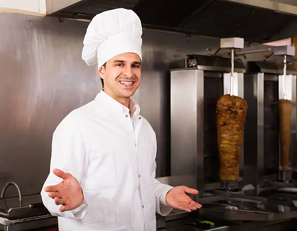 Photo of Positive arabian cook posing near meat for kebab