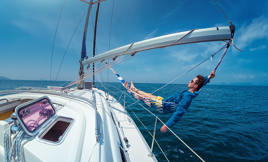 Man relaxing in the hammock set on the sail boat while sailing in the open sea