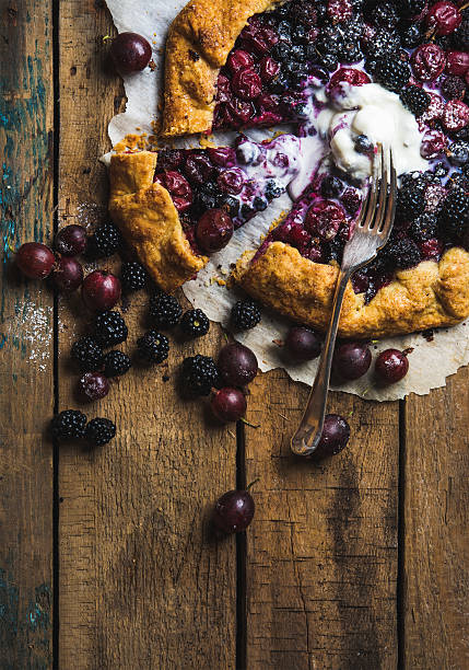 Garden berry galetta sweet pie with melted vanilla ice-cream Homemade garden berry galetta or crostata sweet pie with melted vanilla ice-cream scoop served with fresh berries on rustic wooden background. Top view, copy space, vertical composition crostata stock pictures, royalty-free photos & images