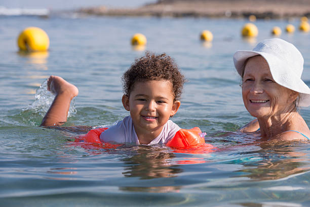 donna addestratore che insegna al bambino a nuotare in mare. - women wading sun hat summer foto e immagini stock