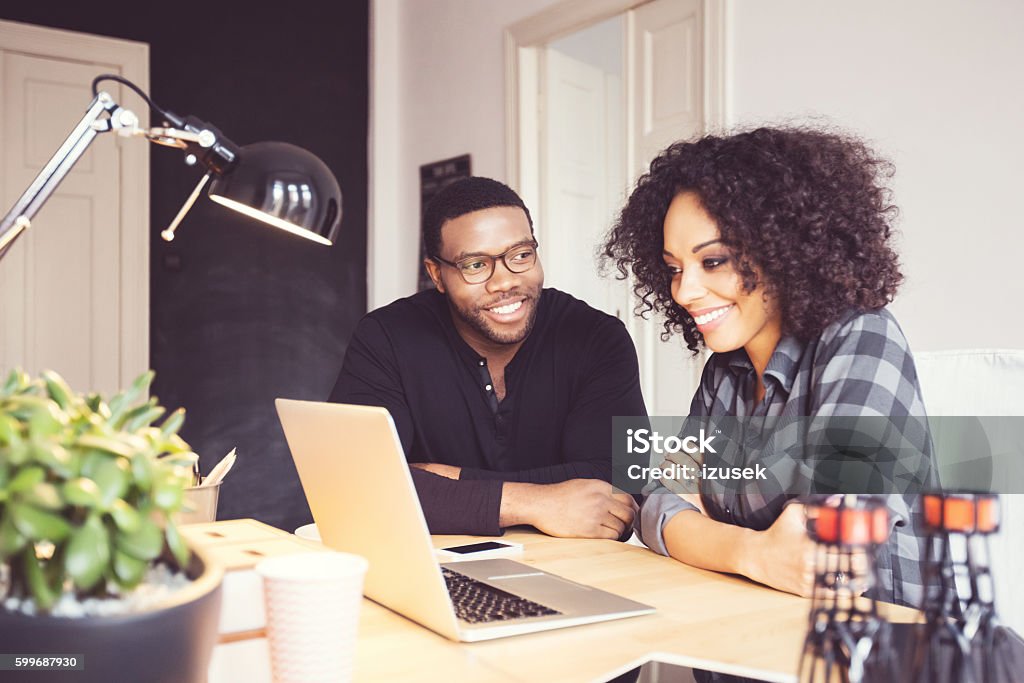 Two designers in the office, using laptop together Afro american young man and woman in the office, using laptop together. Adult Stock Photo
