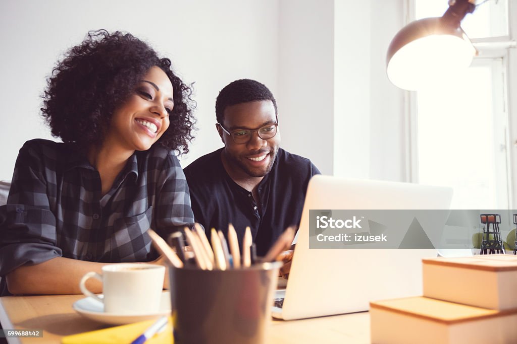 Two designers in the office, using laptop together Afro american young man and woman in the office, using laptop together. African Ethnicity Stock Photo