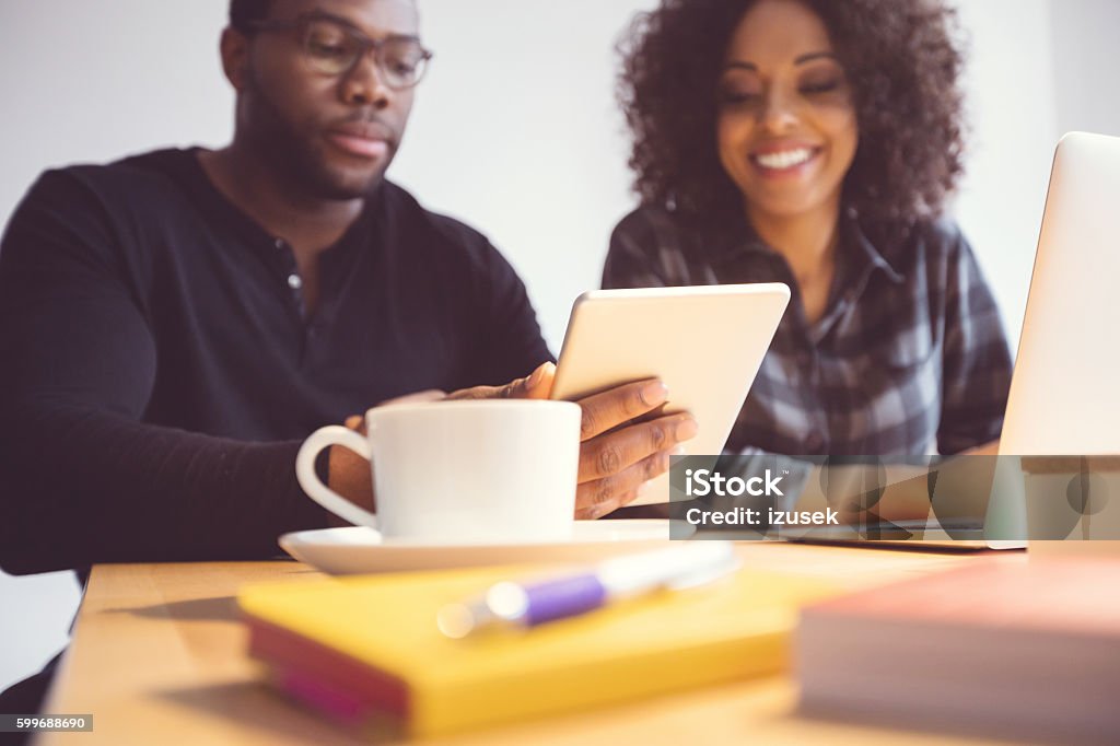 Two designers in the office, using a digital tablet Afro american young man and woman in the office, using a digital tablet together. Adult Stock Photo