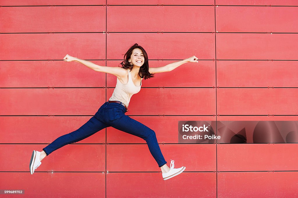 Jumping happy girl Excited girl is jumping against a red wall Happiness Stock Photo