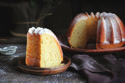 Piece of orange cake sprinkled with powdered sugar on a wooden background