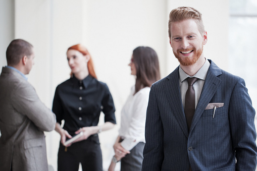A smiling business man stands in front of a group of business people.