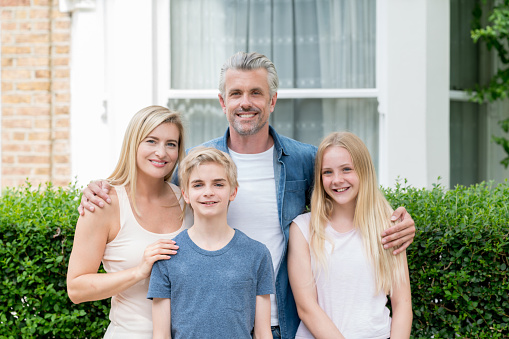 Happy family portrait outside their new house looking at the camera smiling - real estate concepts