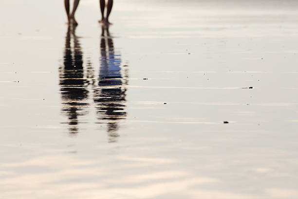 istock Reflection of two people walking in wet sands beach 599755926