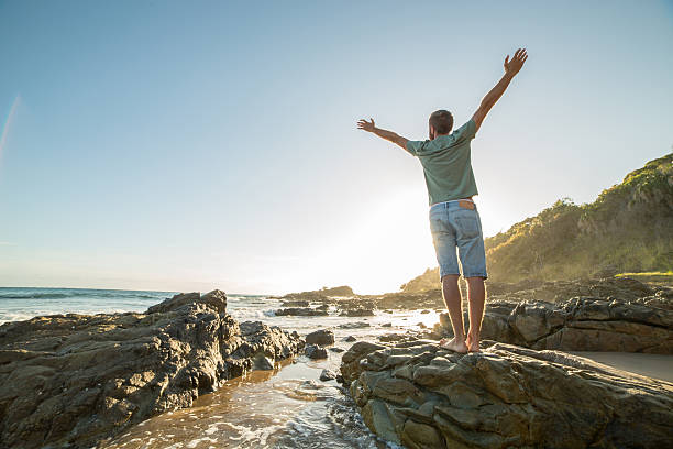 istock Young man arms outstretched on the beach at sunrise 599756640