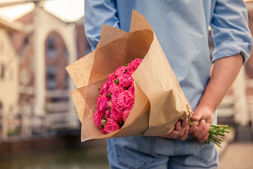 Handsome guy is holding flowers behind his back and waiting for his girlfriend, cropped