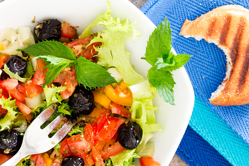 Eating a delicious farm fresh simple Mediterranean salad with black olives and toasted bread with a bite taken out of it on blue napkins, closeup overhead view