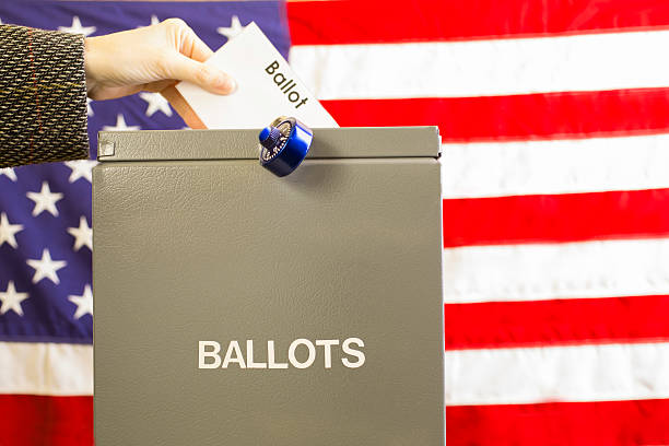 istock Voter inserting ballot into box with USA flag background. 599760132
