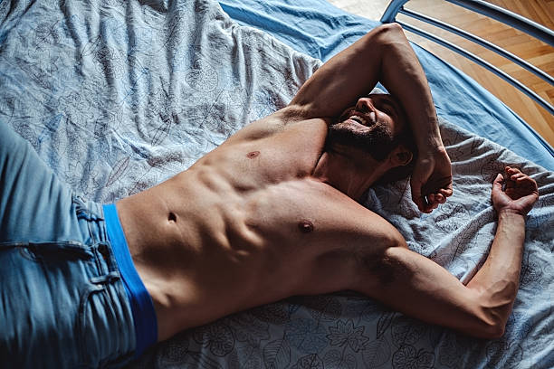 Shirtless man lying in the bad and smiling stock photo