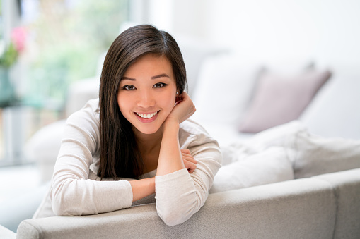 Portrait of a beautiful Asian woman relaxing at home leaning on the couch and looking at the camera smiling