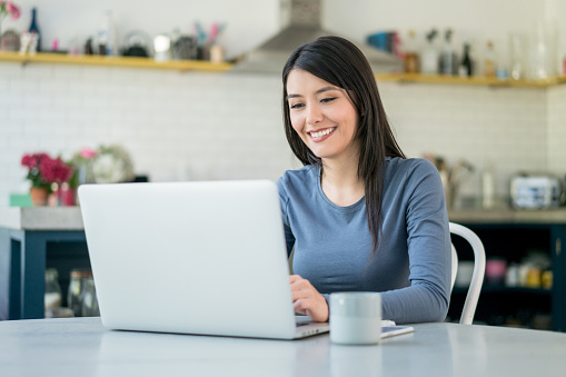Latin American woman at home working online using a laptop computer and looking very happy