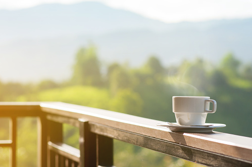 White cup of hot coffee with natural and mountains.