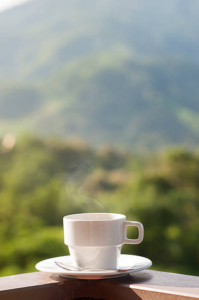 White cup of hot coffee with natural and mountains.