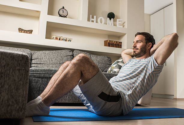 joven atlético haciendo abdominales en la sala de estar. - sit ups fotografías e imágenes de stock